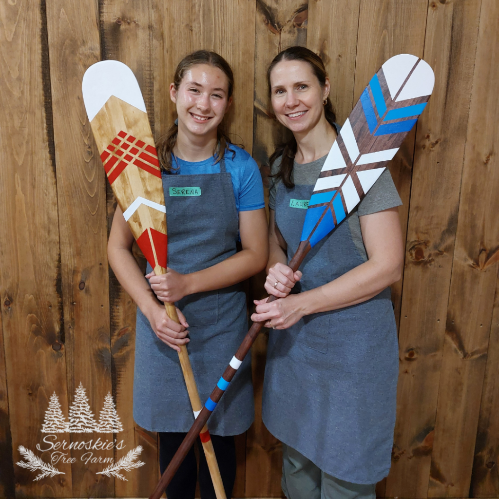 Two people hold completed hand-painted wooden paddles with bold geometric patterns